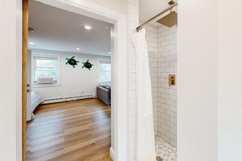 een badkamer met een douche, witte muren en houten vloeren bij Blooming Sunshine - Unit 2 in Falmouth