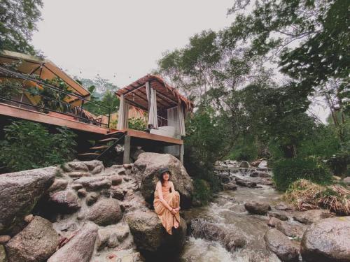 a woman sitting on a rock next to a river at The River whisper in Ban Ton Kham