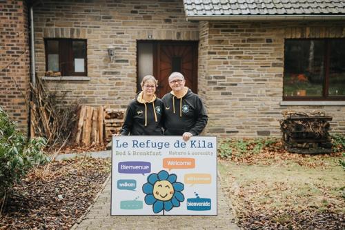 a man and woman holding a sign in front of a house at Le refuge de Kila in Waimes