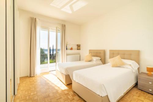 a white bedroom with two beds and a window at Villa dei Lauri - villa vista lago con piscina in Salò