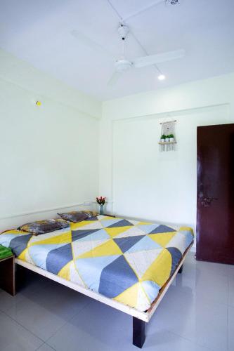 a bed in a white room with a yellow and blue blanket at Nature's retreat villa malavli in Pune