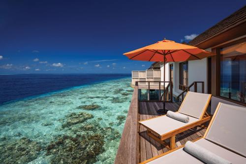 a balcony with chairs and an umbrella and the ocean at OBLU SELECT Sangeli - Premium All Inclusive with Free Transfers in North Male Atoll