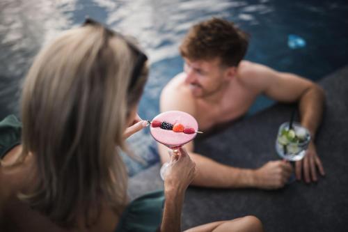 Ein Mann und eine Frau halten einen Drink vor einem Pool. in der Unterkunft Terentnerhof 4*S active & lifestyle hotel in Terenten