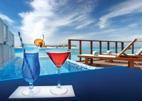 two cocktails sitting on a table next to a pool at OBLU SELECT Sangeli - Premium All Inclusive with Free Transfers in North Male Atoll