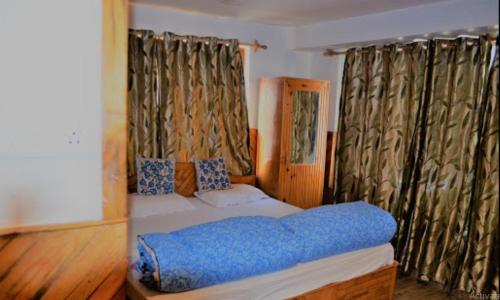a bedroom with a bed with blue sheets and curtains at Hotel The Holy Land in Pahalgām