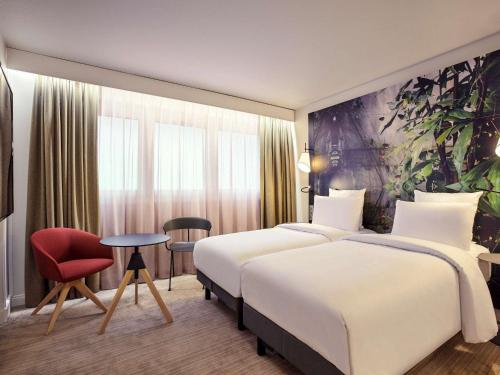 um quarto de hotel com duas camas e uma cadeira vermelha em Mercure Paris La Défense em Courbevoie