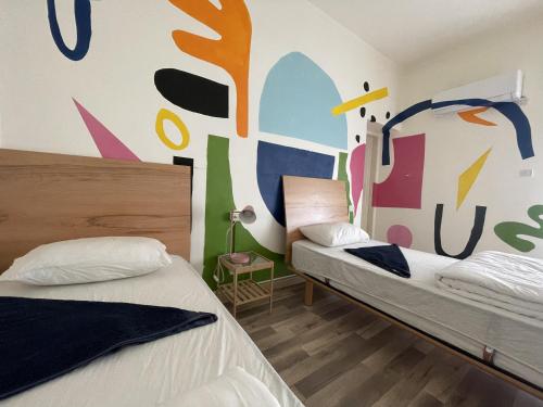 Battuta Hostel في عمّان: سريرين في غرفة مع لوحة جدارية على الحائط