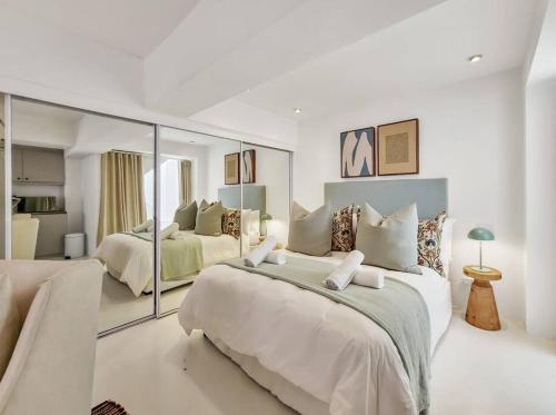 een witte slaapkamer met 2 bedden en een spiegel bij Chic Studio: Exquisite Design, Thoughtful Comforts in Kaapstad