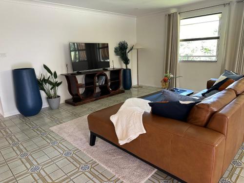 a living room with a brown couch and a television at Amongst the Trees in Mooloolah
