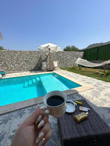 uma mulher segurando uma xícara de café ao lado de uma piscina em Villa Doğa 2 em Fethiye