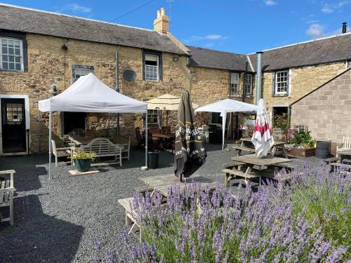 a patio with umbrellas and tables in front of a building at The Plough Inn Leitholm in Coldstream