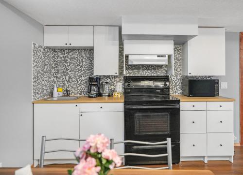 a kitchen with white cabinets and a black stove at Cozy 2-Bedroom Basement Suite Retreat Calgary in Calgary