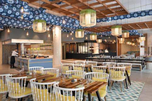 a restaurant with wooden tables and white chairs at Mövenpick Hotel & Apartments Ghala Muscat in Muscat