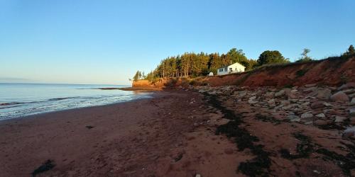 a beach with a house on a hill next to the ocean at Little Eden Summer Beach Home in Long Creek