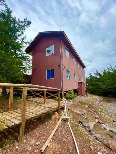 un granero rojo grande con un puente de madera delante de él en hostal el glaciar, en Refugio Lo Valdés