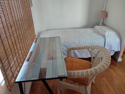 a wooden table with a wicker chair next to a bed at Precioso apartamento a 7 minutos en tren al centro de Valencia in Benetúser