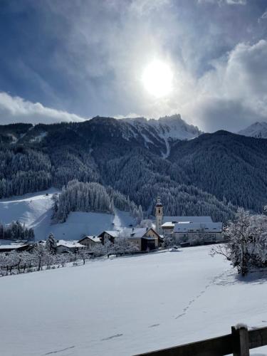 un campo cubierto de nieve con una iglesia y montañas en Ferienwohnung Mondial, en Neustift im Stubaital