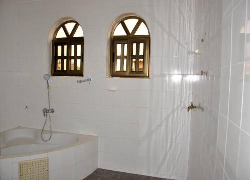 a bathroom with a tub and a sink and two windows at Tatiana City Appartement in Lomé