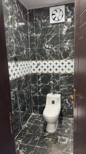 Baño de azulejos negros con aseo blanco en فندق الاقامه السعيده, en Al Bad‘