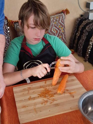 a young boy cutting a carrot on a wooden cutting board at Dar Settash in Fès