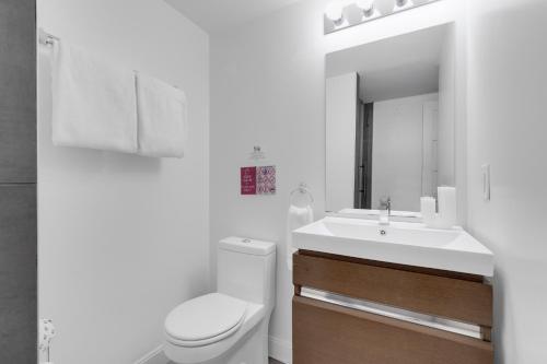 a white bathroom with a toilet and a sink at LiV MTL Main in Montréal