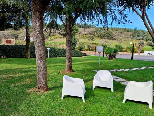 three white chairs and a table in the grass at 3M Hostel & Suites in Alvaiázere