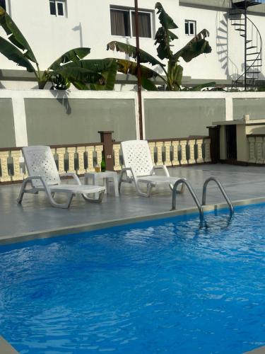two white chairs sitting next to a swimming pool at Villa Familiar con Piscina Privada y Rio in Bonao