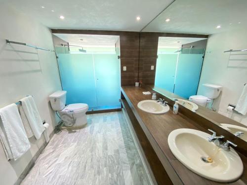 een badkamer met 2 wastafels, een toilet en een spiegel bij Dpto de lujo costera in Acapulco