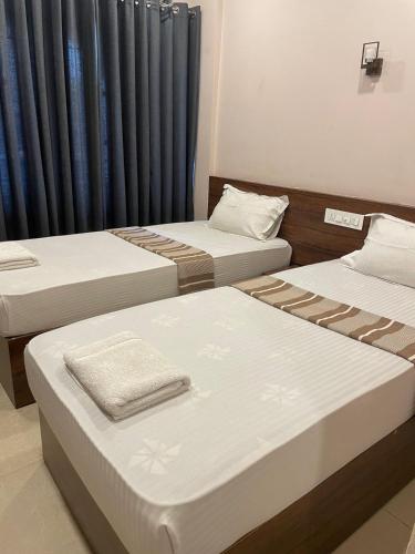 three beds in a room with blue curtains at Plaza Tourist Home in Kannur