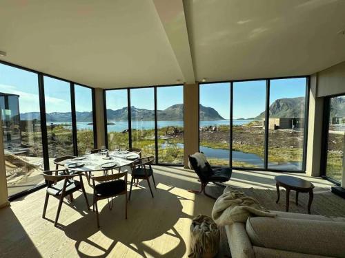 een woonkamer met een tafel en stoelen en glazen ramen bij Designhytte med jacuzzi sentralt i Lofoten in Kleppstad