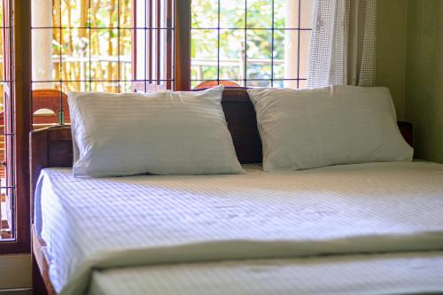 a bed with two pillows on it with two windows at sisi place in Dickwella