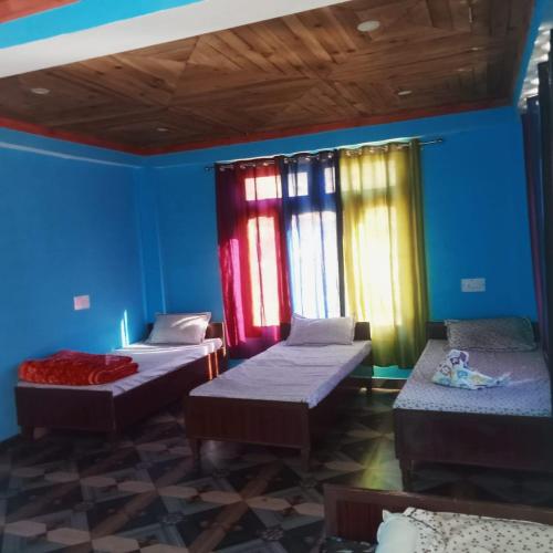 3 łóżka w pokoju z niebieskimi ścianami i oknami w obiekcie Vigyan Guest House Tosh w mieście Tosh