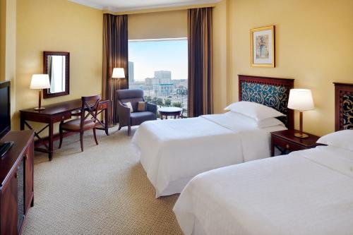 ダンマームにあるシェラトン ダンマン ホテル ＆ コンベンションセンターのベッド2台とデスクが備わるホテルルームです。