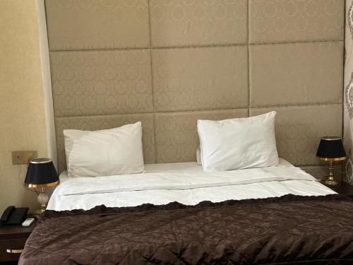 a bed with white pillows and a headboard with two lamps at Sherlock Hotel Baku in Baku