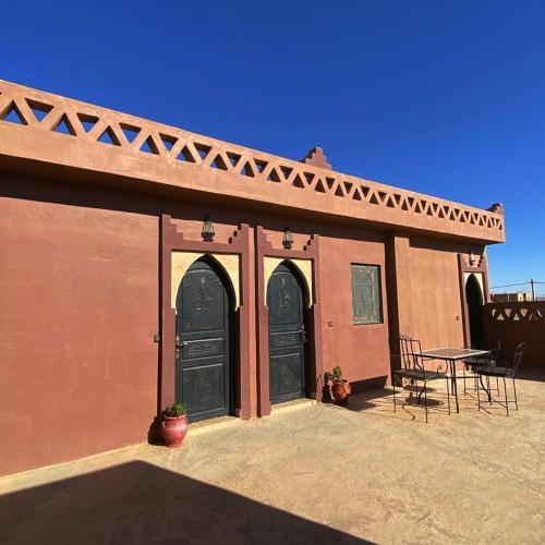 a building with two black doors and a table at Riad Hassi Labied Merzouga in Merzouga