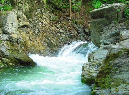 a waterfall on a rocky hillside with green water at Під горою in Sheshory