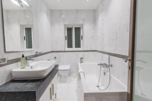 a white bathroom with a sink and a tub and a toilet at Sun Valley Suite - Hosted by Sweetstay in Mosta