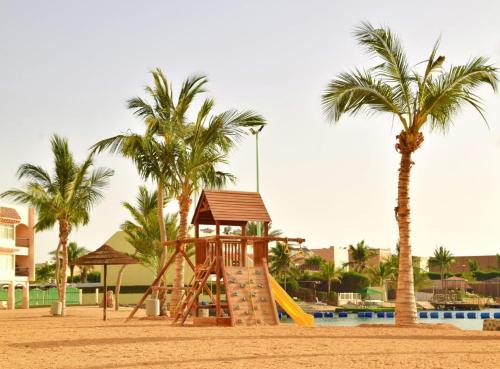 einen Spielplatz mit Rutsche und zwei Palmen in der Unterkunft فاوتشر فان بيتش in Durrat Al-Arus