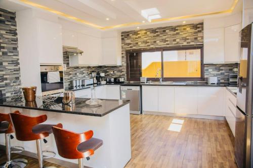 a large kitchen with white cabinets and orange bar stools at Z Apartment (4bedroom) in Lusaka