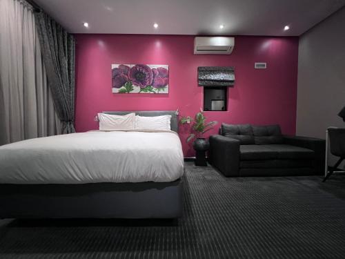 a bedroom with a pink wall with a bed and a couch at The Raz in Harrismith