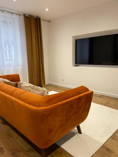 an orange couch in a living room with a flat screen tv at La Fleur de Sel in Honfleur