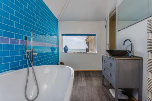 a bathroom with a tub and a sink and blue tiles at Cooden Beach Corner - awesome views! in Bexhill