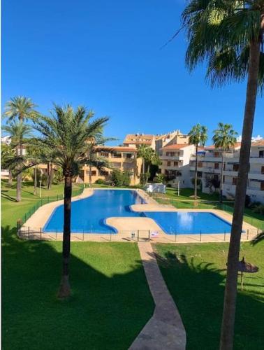 une grande piscine avec des palmiers et des bâtiments dans l'établissement ¡Piso familiar en Jávea!, à Jávea