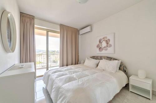 une chambre blanche avec un grand lit et une fenêtre dans l'établissement Eden, à Antibes