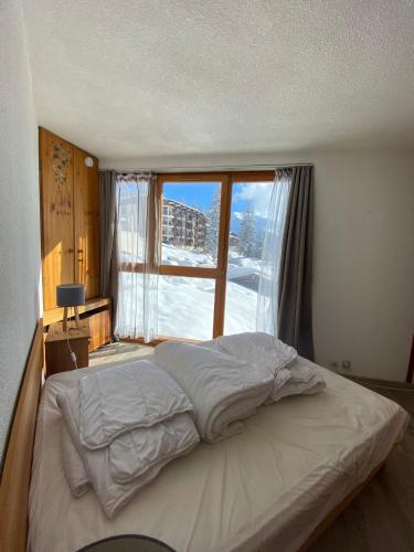 un lit dans une chambre avec une grande fenêtre dans l'établissement F2 front de neige la Rosière, à La Rosière