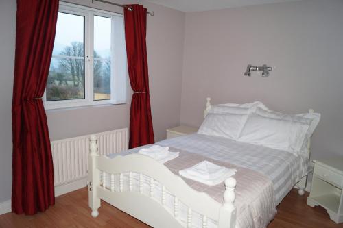 a bedroom with a white bed with red curtains and a window at Clonmurr B&B in Ballyroney