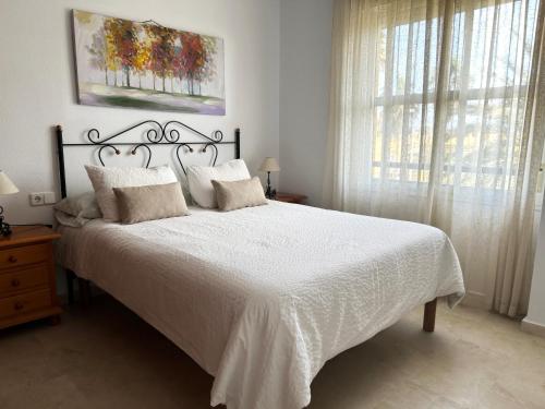 a bedroom with a white bed with white sheets and a window at Ático Barrio de los Pescadores in Costa Ballena