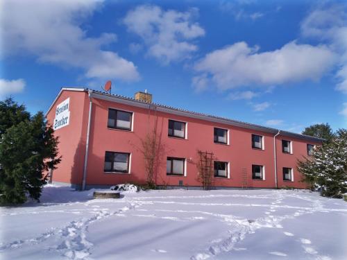 a red building with snow in front of it at Pension Stocker in Dierhagen