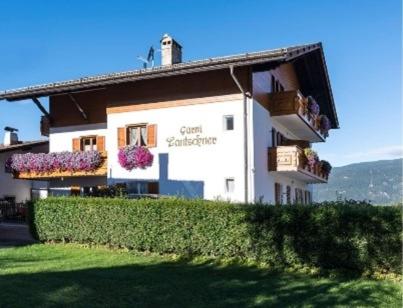 um edifício com flores nas janelas e uma sebe em Garni Lantschner em Kastelruth