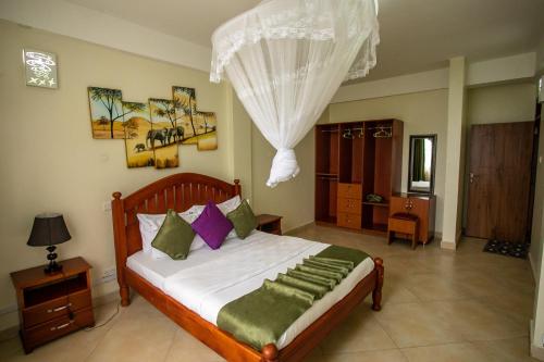 um quarto com uma cama com lençóis brancos e almofadas verdes em ST STEVENS SUITES, ENTEBBE em Entebbe